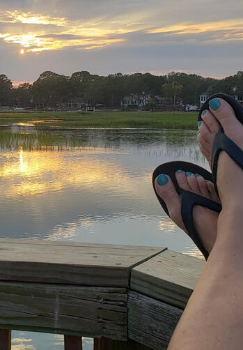 Relaxed view of the water from a crab dock with crossed feet, painted toes, and sandals at sunset