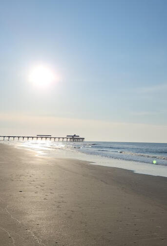 Sun low over the ocean beside Folly Beach Pier on a calm morning.