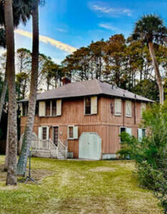The famed Porgy House, a charming raised brick home surrounded by palm trees and greenery.